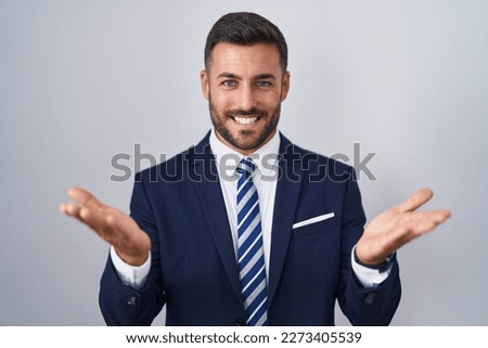 Handsome hispanic man wearing suit and tie smiling cheerful offering hands giving assistance and acceptance.  Royalty-Free Stock Photo #2273405539