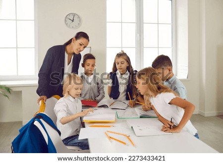 Elementary students having interesting class with teacher. Group of children gather around table in classroom, draw with pencils, make their own stories and learn new skills. Back to school concept
