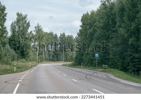 empty asphalt road in green summer forest with trees and grass. perspective, bus stop in Latvia countryside