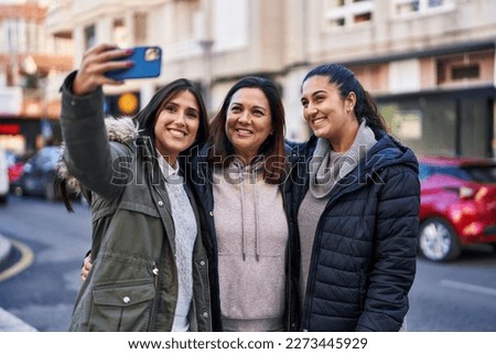 Three woman mother and daughters make selfie by the smartphone at street