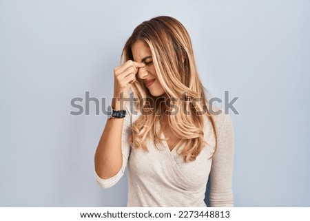 Young blonde woman standing over isolated background tired rubbing nose and eyes feeling fatigue and headache. stress and frustration concept. 