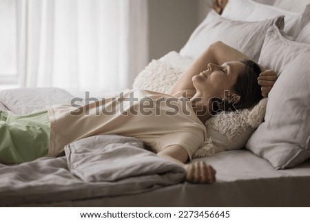 Peaceful serene mature woman enjoying leisure time in comfortable bed, lying on back over blanket, smiling with closed eyes, sleeping, taking break, pause, relaxing, breathing fresh air Royalty-Free Stock Photo #2273456645