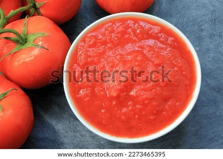 close up of bowl with tomato puree and some tomatoes next to it on gray table Royalty-Free Stock Photo #2273465395