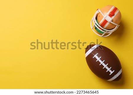 Mini helmet of football player and ball on yellow background  with copy space