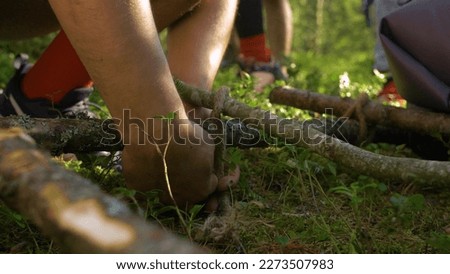 A man ties branches with a thick rope, making a stretcher. Hiking in the coniferous forest. Close-up of the hands. Royalty-Free Stock Photo #2273507983