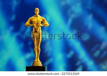 Hollywood Golden Oscar Academy award statue on light rays on blue background with copy space. Success and victory concept.