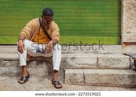 A good looking black man is taking a break after hanging out and taking pictures in the city, all day
