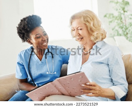 Doctor or nurse caregiver with senior woman looking at photo album and picture or book or brochure at home or nursing home
