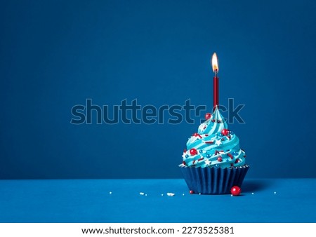 Blue cupcake with red sprinkles and lit candle on a blue background. Royalty-Free Stock Photo #2273525381