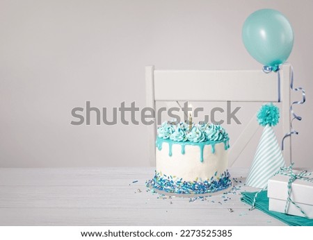 Blue Birthday cake, presents, hats and balloons over light grey background.