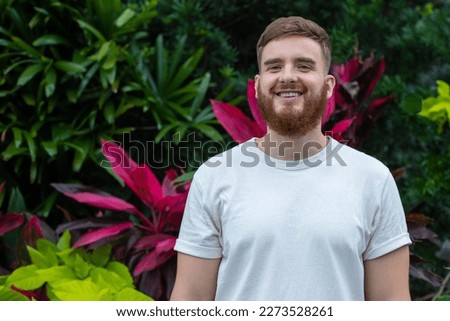 Portrait of happy young bearded man with beard breathing deep, inhale fresh air on natural background, green wall with leaves, flower in tropical country in garden. Eco, ecological concept. 