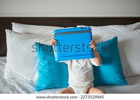 Cute little Asian 2 years old toddler baby boy child wearing diaper lying in bed watching a video from tablet pc. Kids playing with tablet computer, Gadget-addicted children