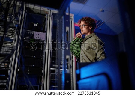 Data center engineer with many optic wires cables walking next to computer racks