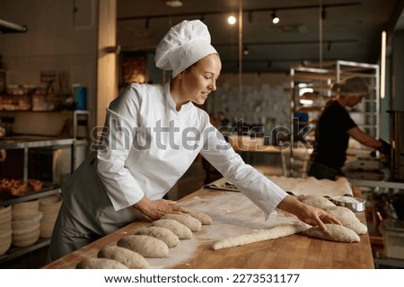 Woman baker forming bread loaves from raw dough at professional kitchen Royalty-Free Stock Photo #2273531177