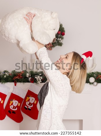 beautiful girl stands near the Christmas decorations fireplace and playing with teddy beer