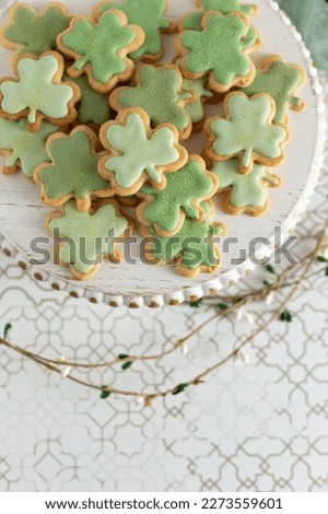 Top View of Decorated Shamrock Cookies on a White Pedestal on Gold and White Background