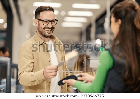 A smiling man is purchasing with credit card on pos terminal at checkout.