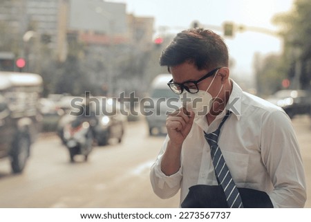 Business man wearing a mask and coughing on the street. Protection against air pollution and dust particles exceeds safety limits.PM2.5 unhealthy air pollution dust smoke in the urban city, PM 2.5 Royalty-Free Stock Photo #2273567737