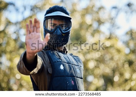 Man, paintball and hands in stop signal for team communication or strategy on the battlefield in nature. Male paintballer or soldier showing hand sign halt or wait in adrenaline sport outdoors