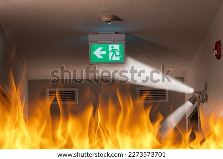 Photo illustration of emergency exit sign with fire in hallway of modern building for a concept of fire escape safety planning and preparation