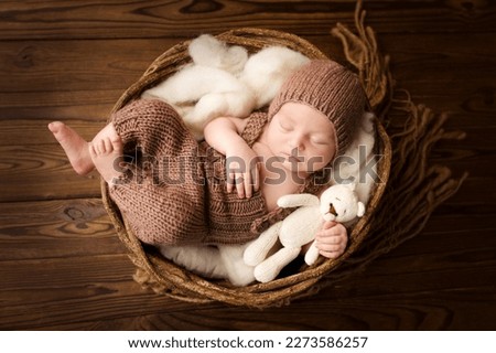 Top view of a newborn baby sleeping in a brown overalls, in a brown knitted cap, on a white felt flokati. On a dark wooden background. Beautiful portrait of a little newborn 7 days, one week old.