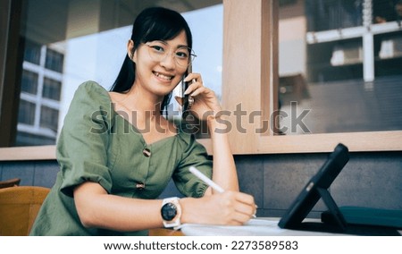 Smiling designer Asian girl  in casual clothing wear glasses using tablet computer connected to wifi, cheerful female freelancer enjoying working while working remotely.