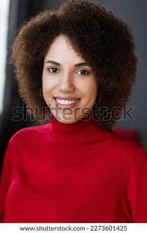 Authentic portrait of attractive happy African American woman. Smiling curly haired student wearing  red turtleneck sweater looking at camera