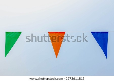 Colourful flag waving in the air on sky with selective focus, Multicolour of pennant flags (green, orange and blue) hanging on the rope with clear sky background. Free copy space for your text.