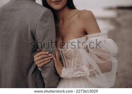 Close up of bride with ring hugging groom at beach, seaside. Woman wearing wedding dress smiling, getting married with man wearing costume. Concept of marriage and family relations. Royalty-Free Stock Photo #2273613029