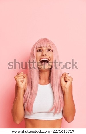 Pretty young woman smiling enjoying life rejoicing a win feeling happy, friendly, satisfied and carefree with hand raised up, isolated next to pink background. Winner concept