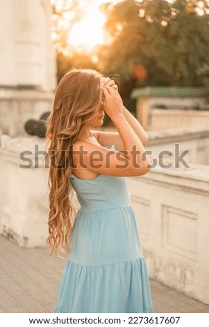 Woman sunset blue dress. Portrait of a woman with long hair and a blue dress against the backdrop of the setting sun and a white building. Lifestyle, walking around the city