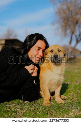 a beautiful dark-haired girl, in a black sweater spends time with a dog, a homeless dog, friends lie on the grass in the yard, hugging, taking pictures on the phone.the girl cares about a homeless dog