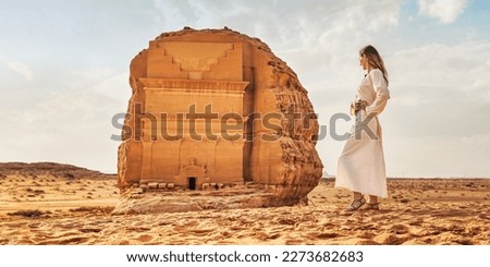 Young Caucasian woman in long white dress posing in front Tomb Lihyan Son of Kuza or Qasr al-Farid at Hegra, Saudia Arabia, sandy desert landscape around. Saudi Arabia opened to tourism in 2019 Royalty-Free Stock Photo #2273682683