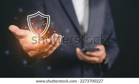 Businessman holding shield protective icon. Smartphone network security protection and data security concept, cyber security and hazard protection.