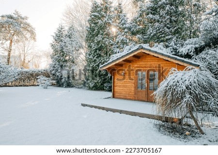 Small wooden house surrounded by many trees and snow. Winter holidays in Scandinavia, Norway or Sweden. Winter mood in the garden. Garden house for cosiness in the village Royalty-Free Stock Photo #2273705167