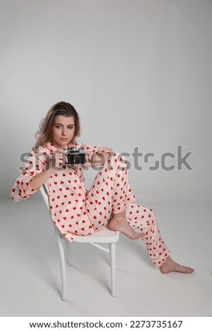 a beautiful blonde girl on a white background in pajamas takes pictures on an old camera. pajamas with hearts. Valentine's Day. heart print pajamas. clothes for sleep and home