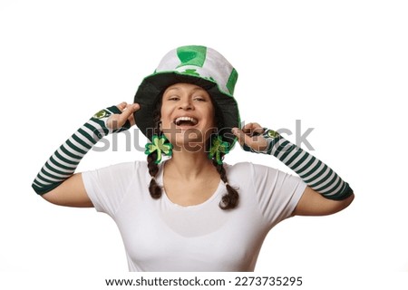 Portrait on white background of a middle-aged attractive pretty woman in Saint Patrick's hat and clover leaves earrings, smiling with a beautiful smile looking at camera. Irish culture and traditions