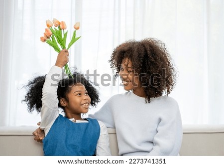 Nice girl and her mother enjoy sunny morning. Good time at home. Child giving card flower for her mom. Family playing on sofa.