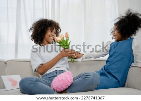 Nice girl and her mother enjoy sunny morning. Good time at home. Child giving card flower for her mom. Family playing on sofa.