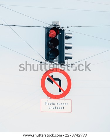 Two hanging traffic lights from the city of Copenhagen above a traffic sign that prohibits turning left.