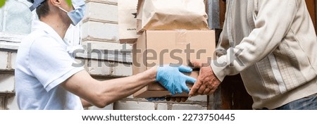 An elderly woman using a walker receives meals from a man working with a benevolent group delivering food to those who are at high risk because of the coronavirus COVID19. Royalty-Free Stock Photo #2273750445