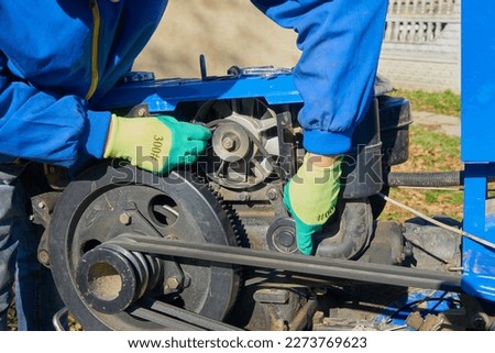 worn out belt replace the generator,repairing a two-wheeled tractor, a man removes the belt from the pulley Royalty-Free Stock Photo #2273769623