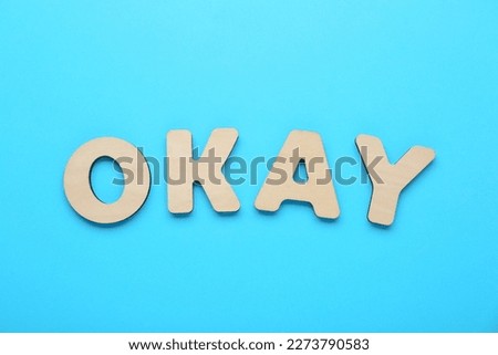 Word Okay made of wooden letters on light blue background, top view