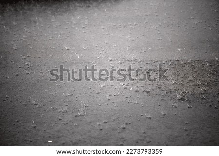 Heavy rain falling on the asphalt, puddles with splashes from drops.