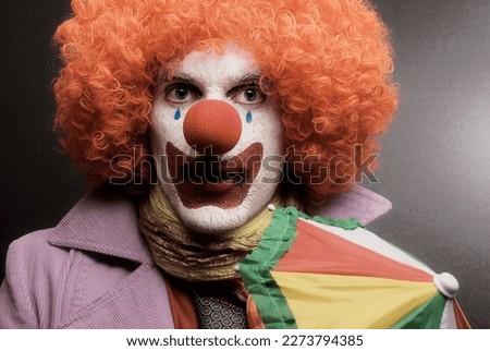 A clown in a red wig with a red nose and an astonished face studio photo