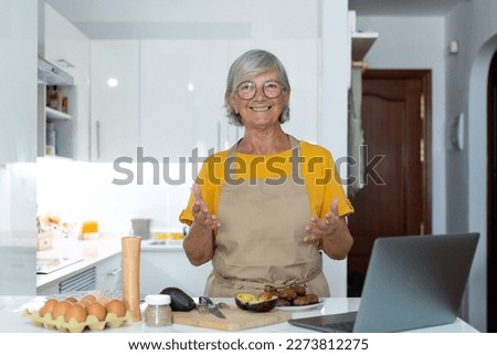 Portrait headshot of old mature woman cooking and preparing meal talking to the camera explaining her recipe to the internet online using laptop.