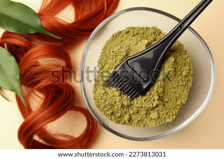 Bowl of henna powder, brush, green leaves and red strand on beige background, flat lay. Natural hair coloring