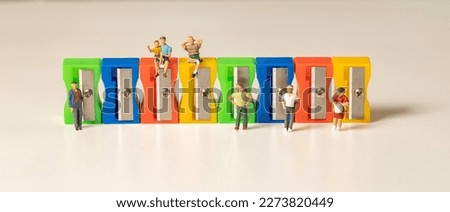 Miniature people at a wall of pencil sharpeners, isolated on white.  Colorful abstract image.