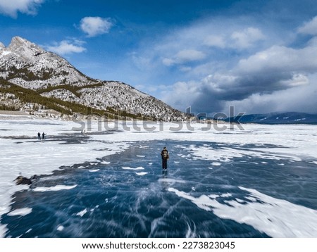 aerial view of a man with beard in sweater man skates on blue ice of abraham lake on ice skates in jasper and banff national park