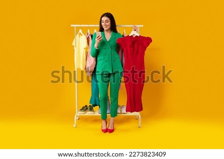 App for online shopping. Young european lady using cellphone and holding dress, ordering clothes online in mobile app over yellow studio background, full length Royalty-Free Stock Photo #2273823409